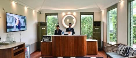 A reception area with a wooden reception desk, a television mounted on the wall, and a sofa.