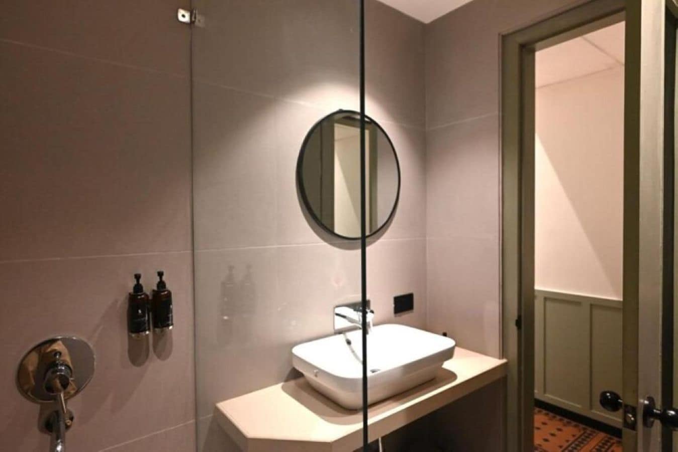 Une salle de bain avec un lavabo blanc, un miroir rond et deux bouteilles de savon accrochées au mur.