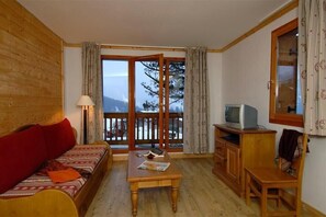 Relax in a serene space with a sofa, wooden table, and large window offering a view of the surrounding landscape.