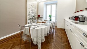 Un coin repas avec une table ronde dressée pour quatre personnes, entourée de chaises. Un paravent décoratif orné de motifs floraux se trouve derrière la table.