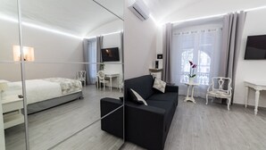 Une chambre d’hôtel moderne avec un lit, un canapé noir, une télévision, une petite table et un miroir.