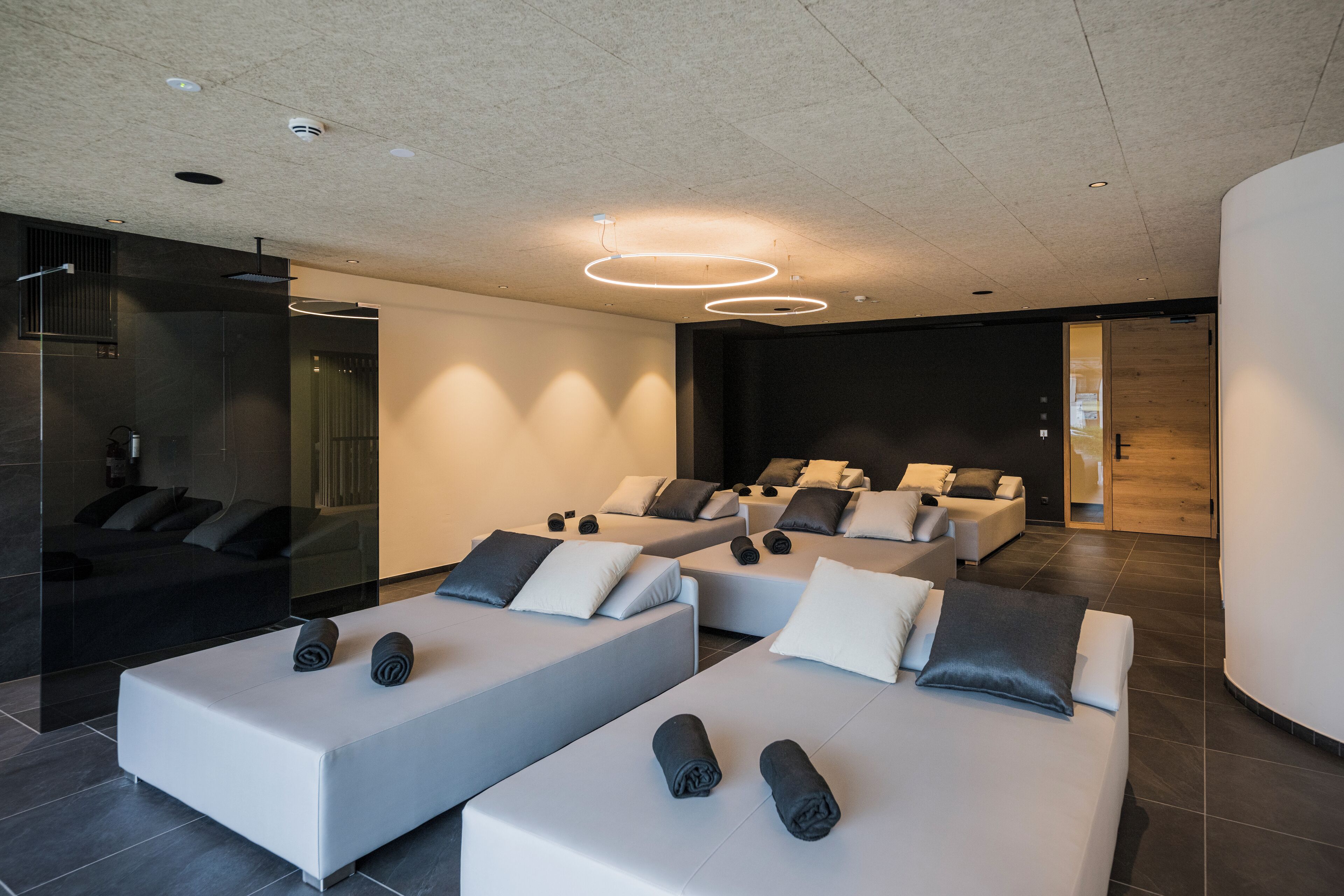 A modern spa with multiple massage tables arranged in a row, a glass-enclosed sauna, and a minimalist design with neutral colors.