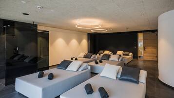 A modern spa with multiple massage tables arranged in a row, a glass-enclosed sauna, and a minimalist design with neutral colors.