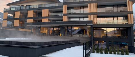 Un hotel moderno de varios pisos con fachada de vidrio, zona de estar al aire libre y suelo cubierto de nieve.