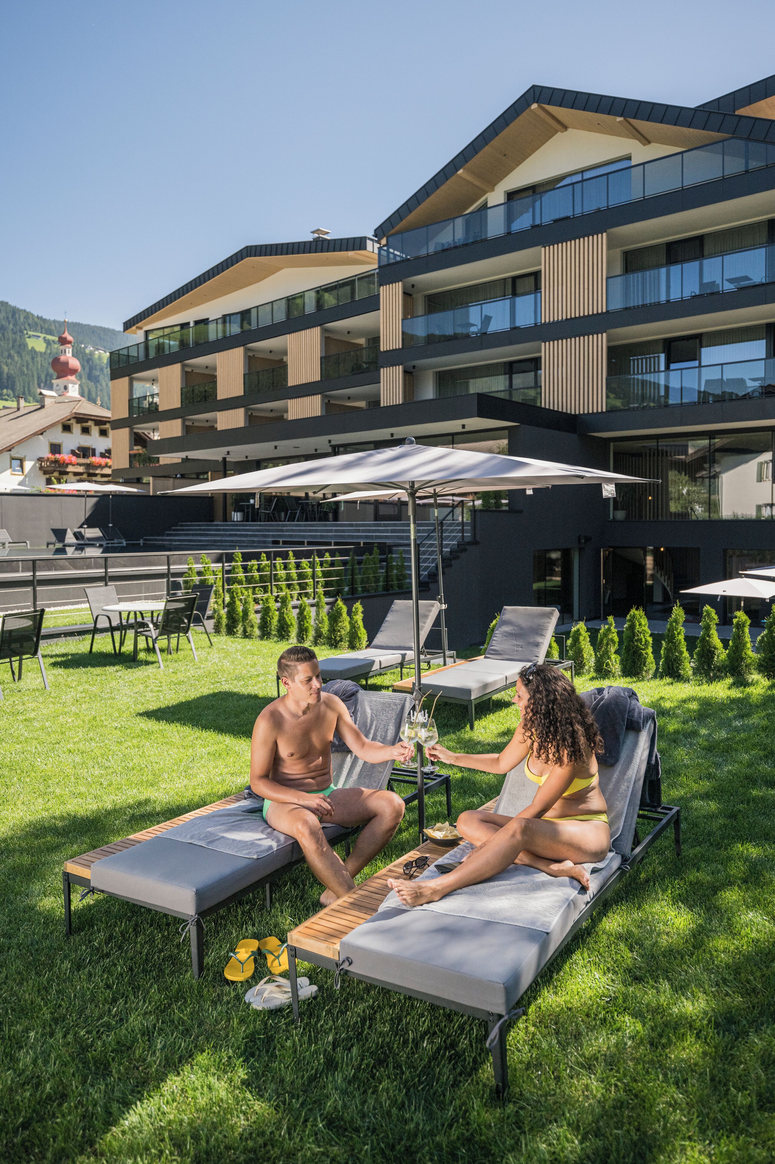 A modern outdoor lounge area with sun loungers, a pool table, and a view of a multi-story building with balconies.