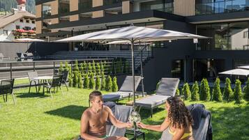 A modern outdoor lounge area with sun loungers, a pool table, and a view of a multi-story building with balconies.