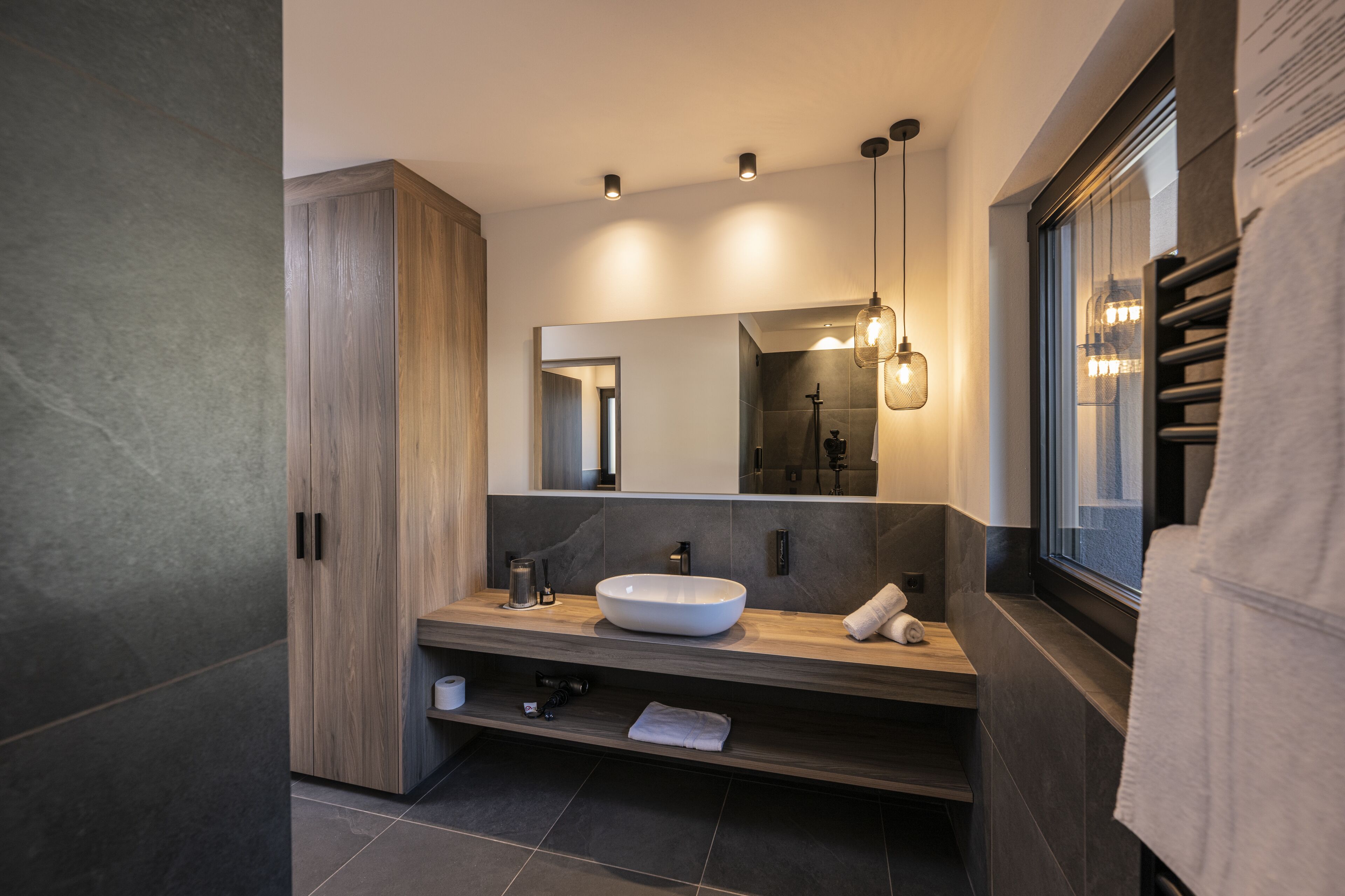Een moderne badkamer met een groot houten kastje, een wastafel en een grote spiegel.