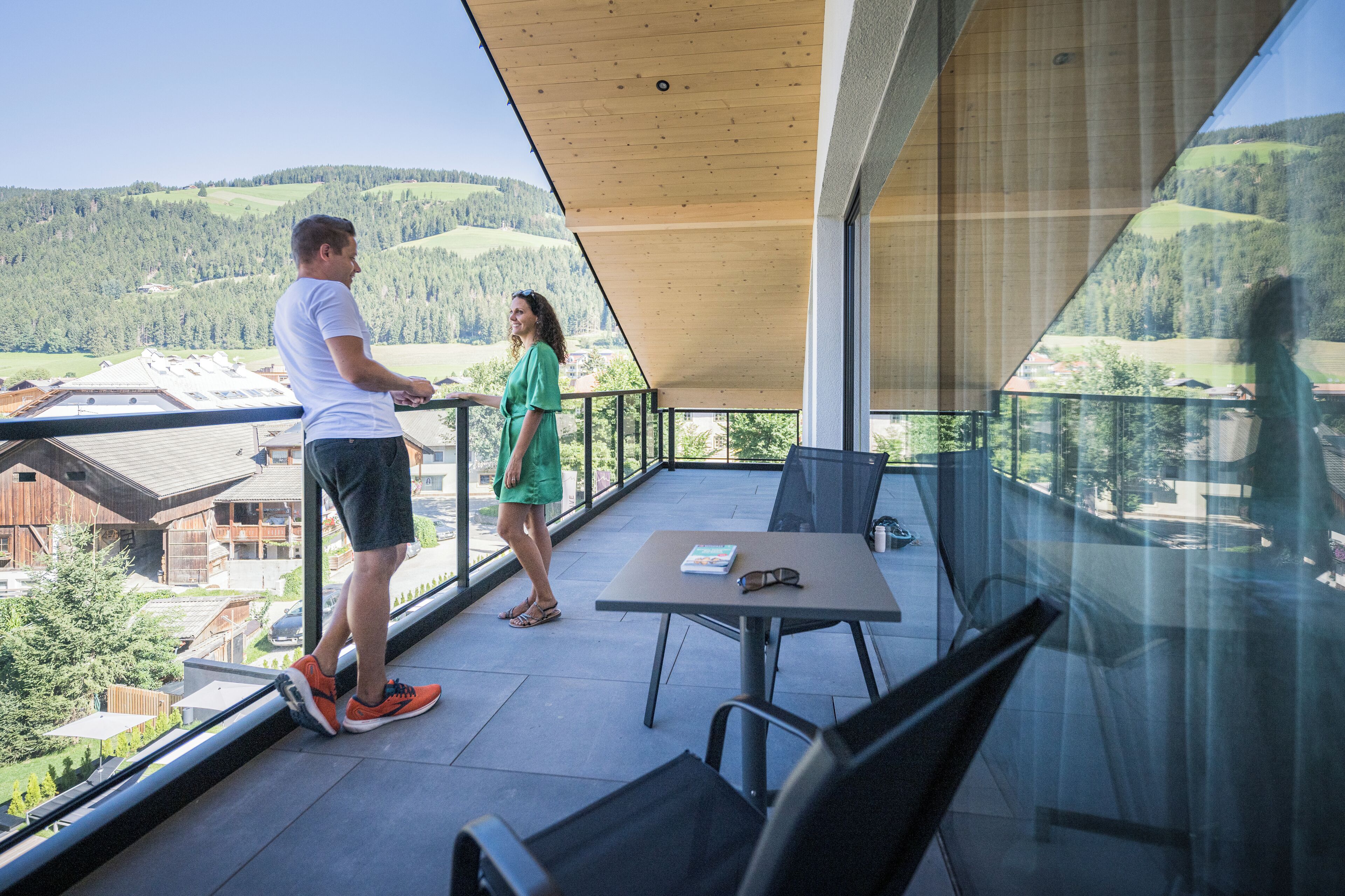 A balcony with a table and chairs, overlooking a scenic landscape with hills and buildings.