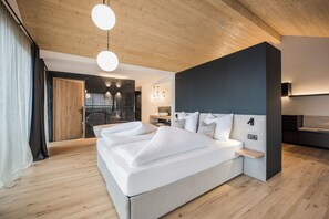 A modern bedroom with a large bed, wooden flooring, and a stone fireplace. - Montanaris Apartments (Villabassa)