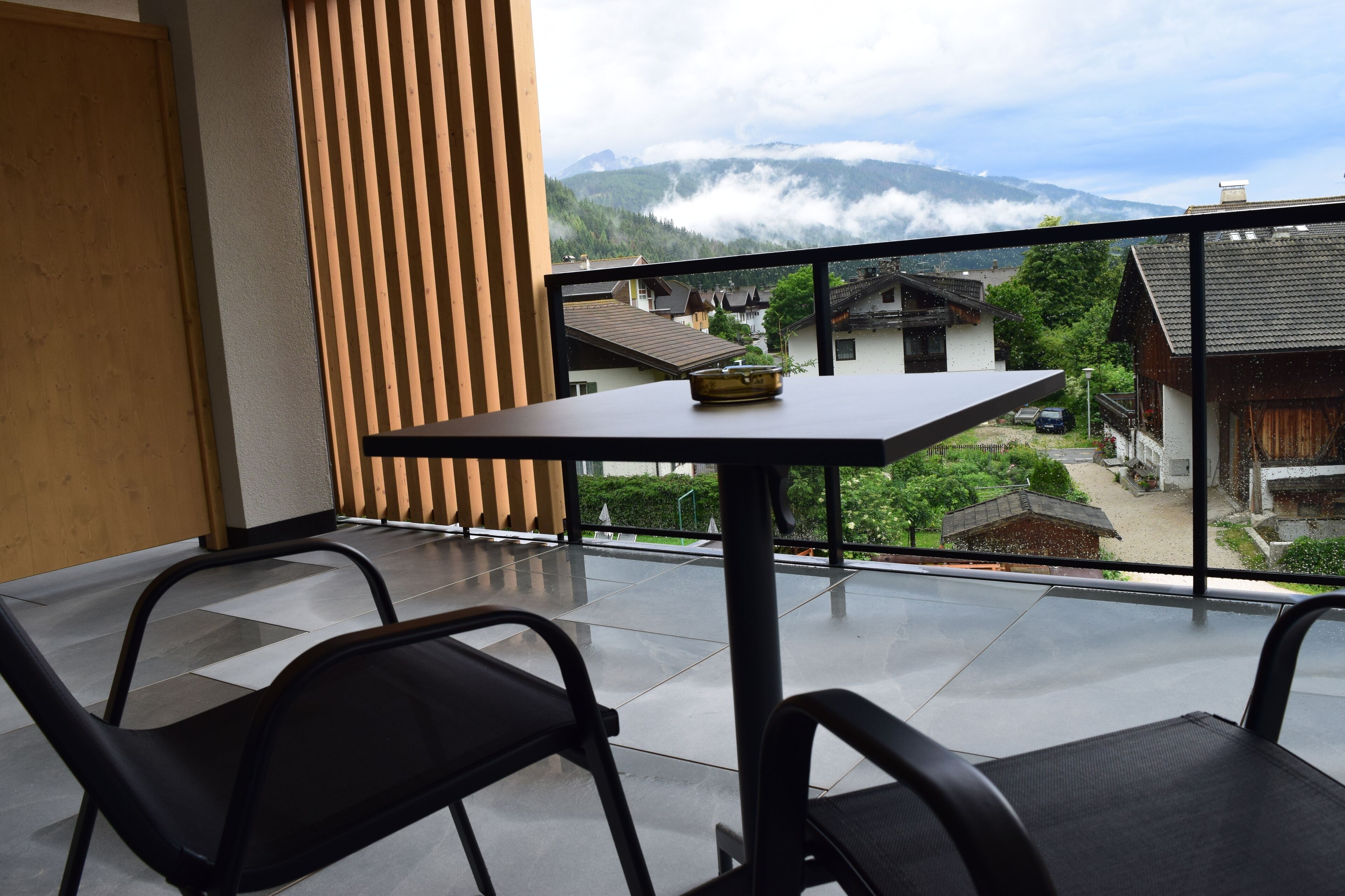 Een balkon met een tafel en stoelen, met uitzicht op een dorp en bergen.
