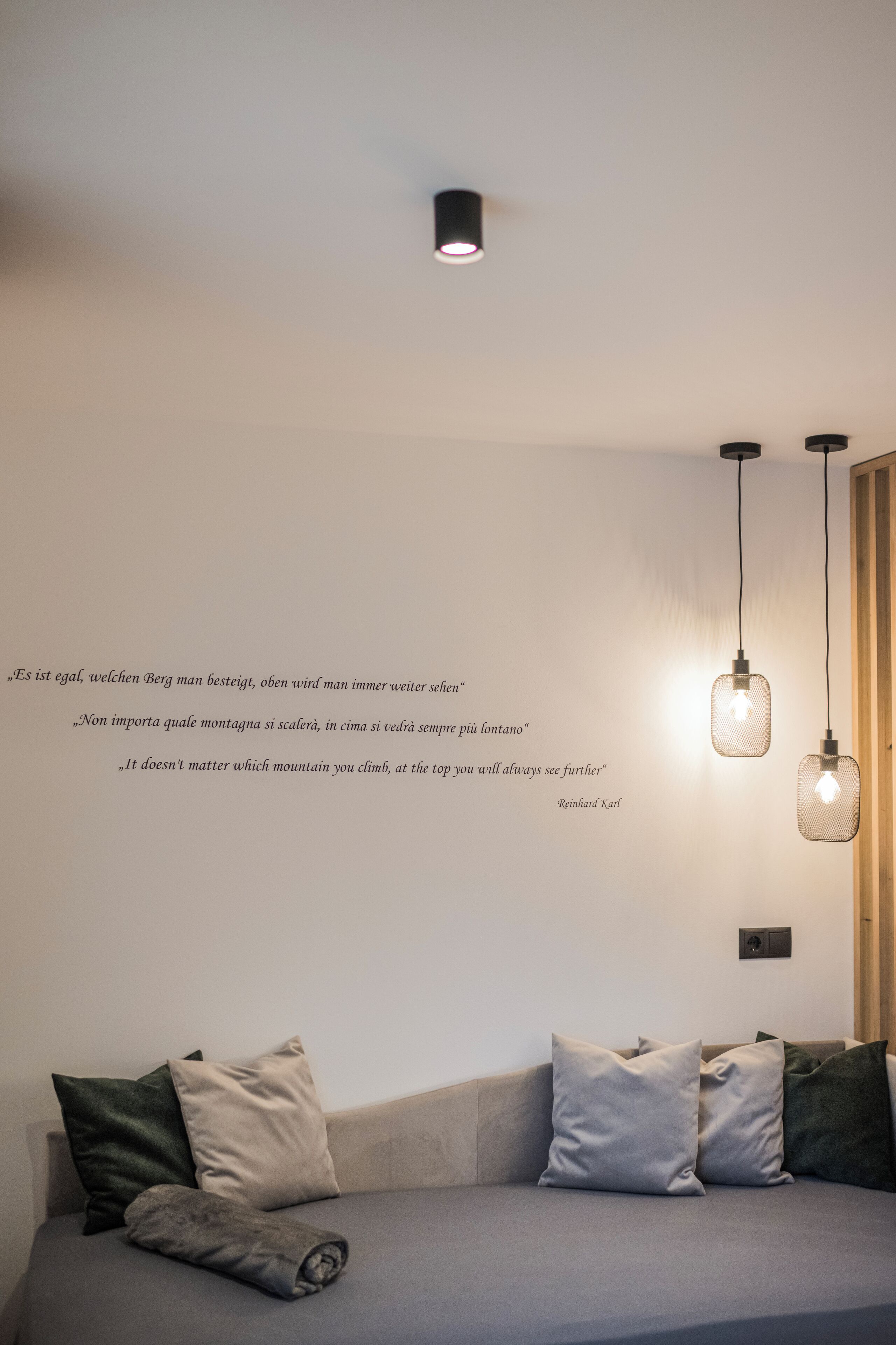 A modern room with a grey sofa, multiple cushions, and a wall with inspirational quotes.