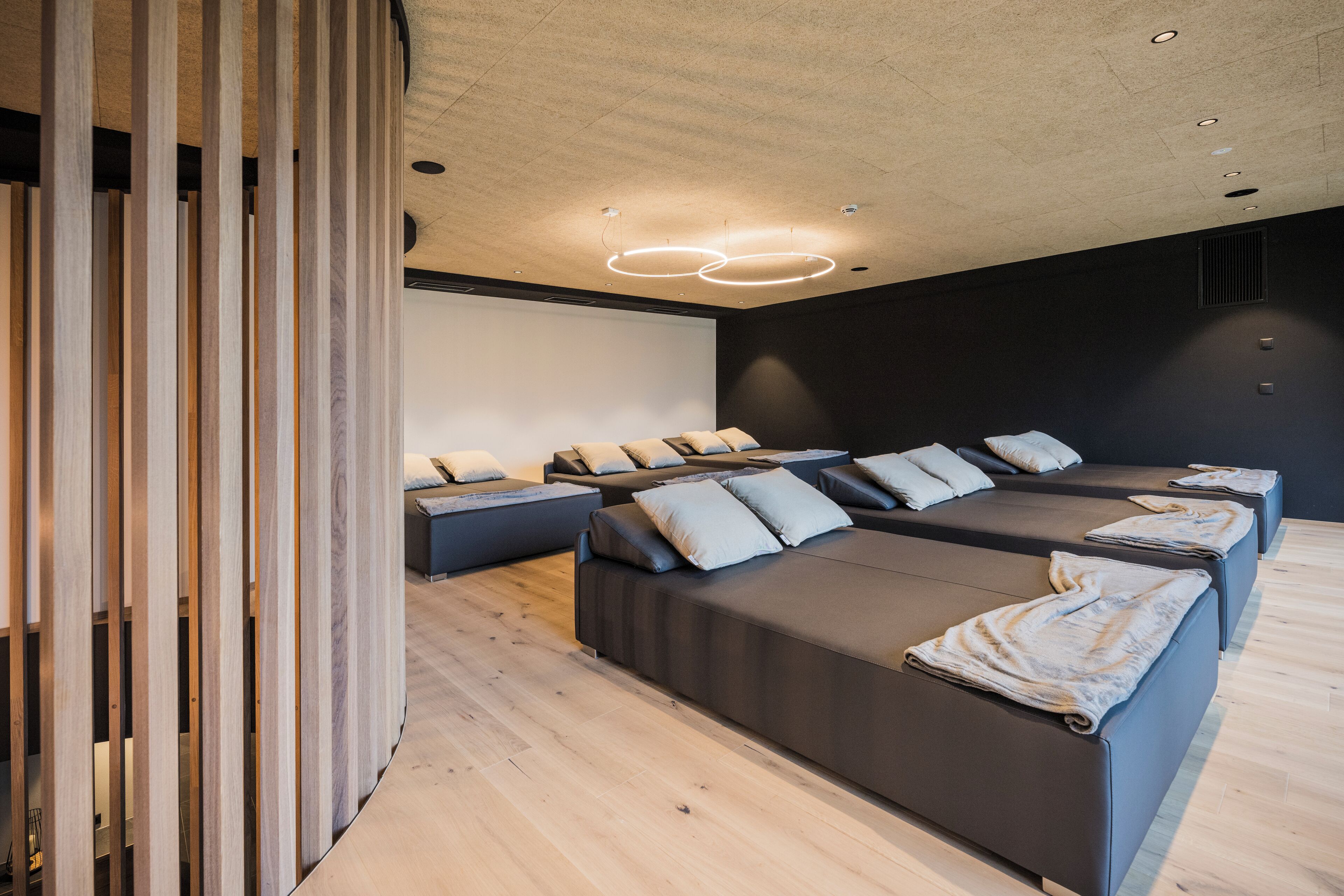 A modern spa room with multiple massage beds, wooden partitions, and a ceiling with recessed lighting.