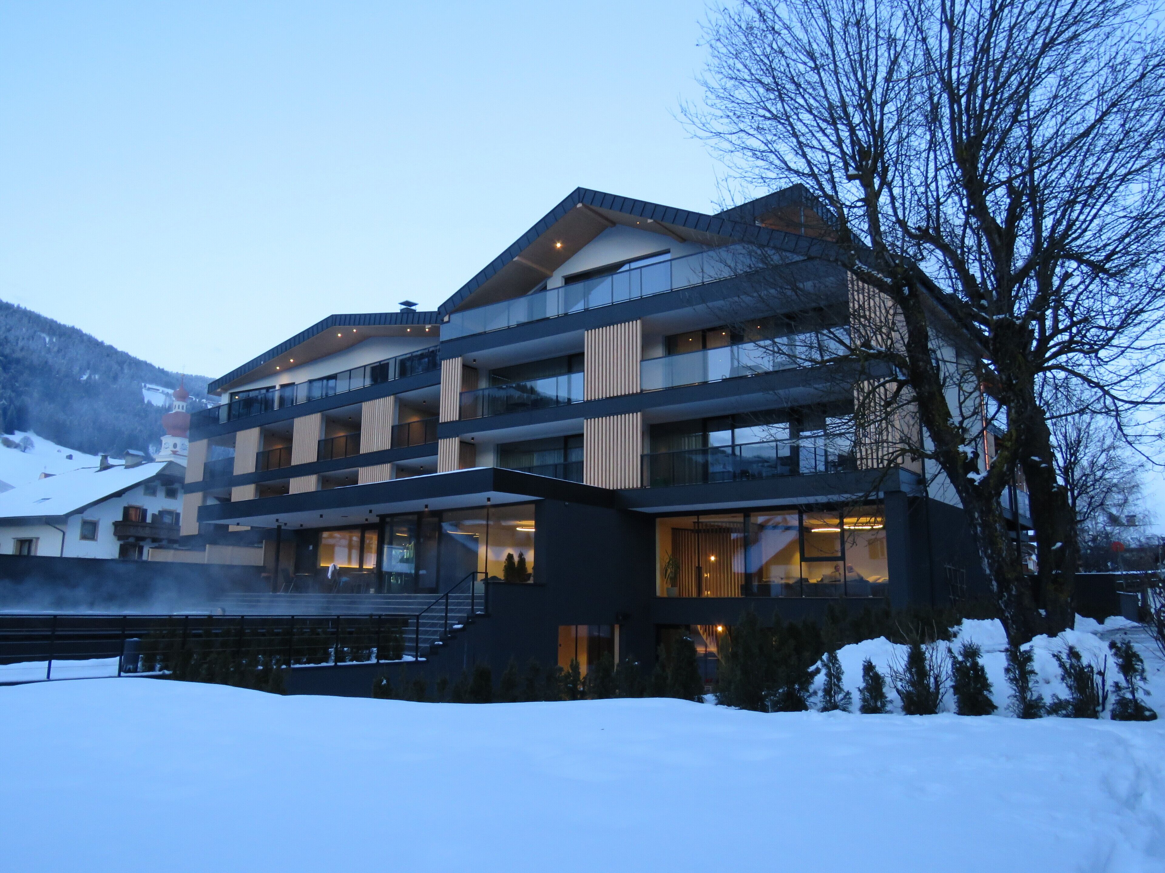 Un hotel moderno de varios pisos con balcones y ventanas amplias, rodeado de nieve y árboles.