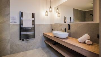 Un baño moderno con tocador de madera, un lavamanos blanco y un perchero para toallas.