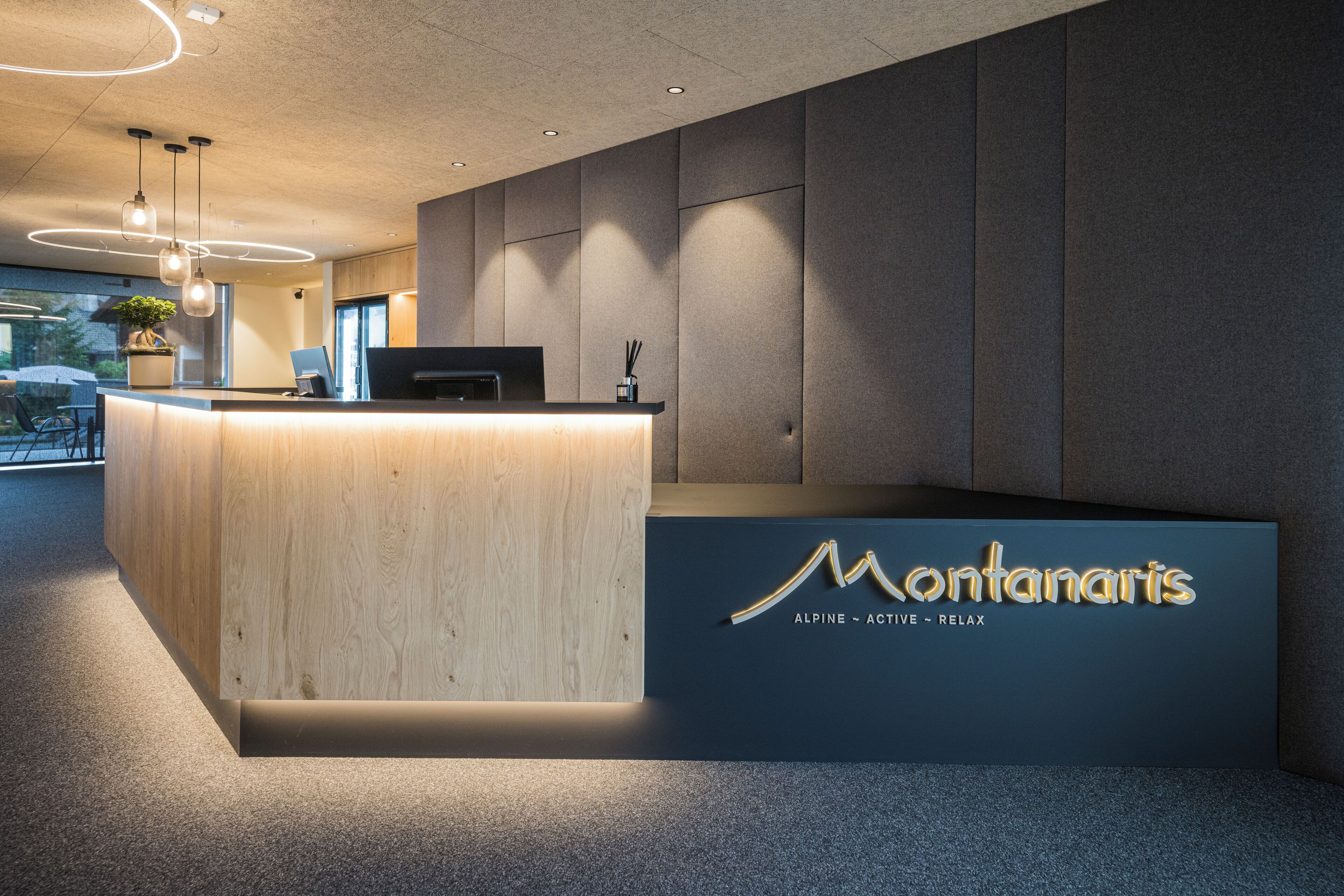A reception desk with a wooden finish and a dark blue sign that reads "Montanaris" with the words "ALPINE - ACTIVE - RELAX" underneath.