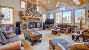 A cozy living room with a stone fireplace, large windows, a television, and comfortable seating. - Boulder Lodge At Peak 8 4 Bedroom Home by RedAwning (Breckenridge)