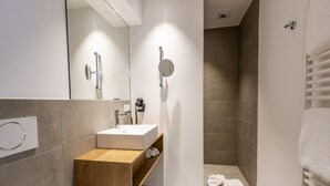 Un baño moderno con tocador de madera, lavamanos blanco y cabina de ducha de vidrio.