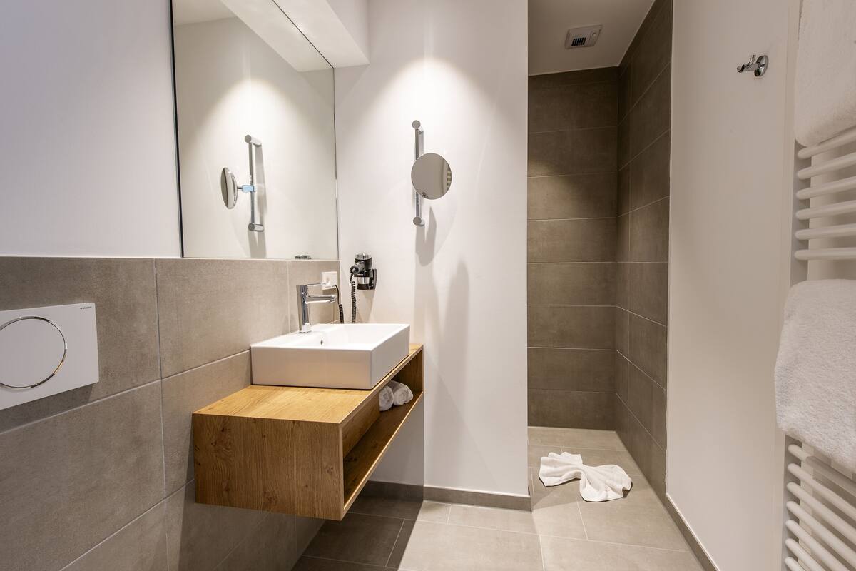 A modern bathroom with a wooden vanity, a white sink, and a glass shower enclosure.