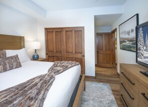 Un dormitorio con una cama, una mesita de noche, un armario de madera, un aparador y un cuadro en la pared.