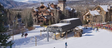 A ski resort with wooden buildings, a ski lift, and a snowy mountain backdrop.