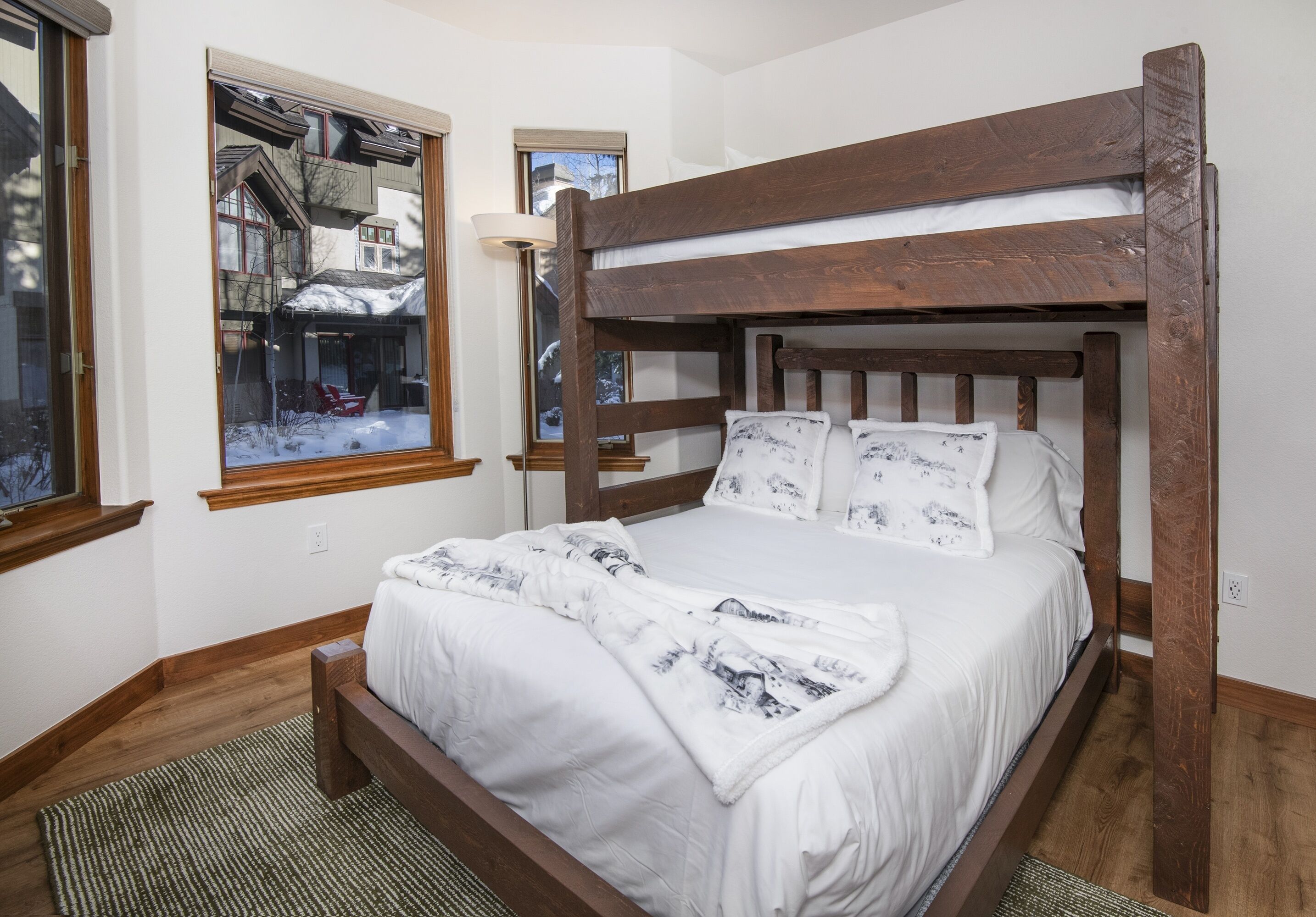 A wooden bunk bed with white bedding and a view of a snowy village through a window.