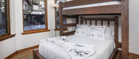 A wooden bunk bed with white bedding and a view of a snowy village through a window.