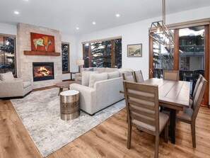 A modern living room with a fireplace, large windows, and a dining area. - Aspenwood 102 2 Bedroom Condo by RedAwning (Edwards)