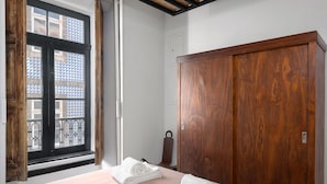 A bedroom with a large wooden wardrobe, a bed with a pink bedspread, and a window with a view of buildings. - National Theater Houses 20 (Porto)