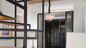 A modern living room with a wooden ceiling, a black-framed sofa, a patterned rug, and a chandelier. - National Theater Houses 20 (Porto)