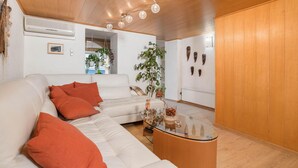 Ein modernes Wohnzimmer mit einem weißen Sofa, orangefarbenen Kissen, einem Glastisch und einer Holzbalkendecke.