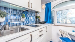 Eine kleine Küche mit Spüle, Herd und Schränken, ein Fenster mit Blick und ein blauer Vorhang.
