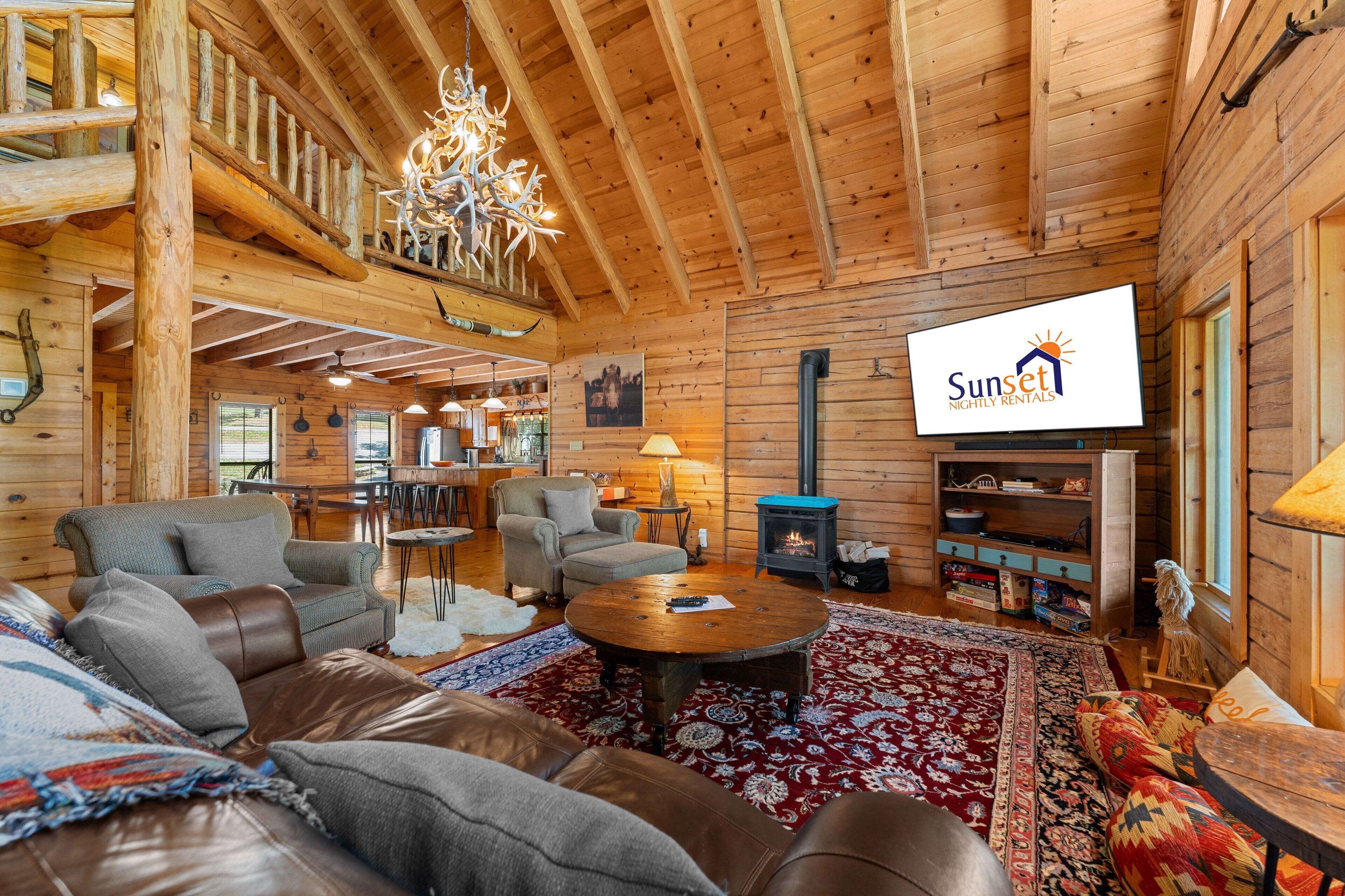 Interior acogedor de una cabaña de troncos, con chimenea, muebles de madera y un televisor que muestra 'Sunset Nightly Rentals'.