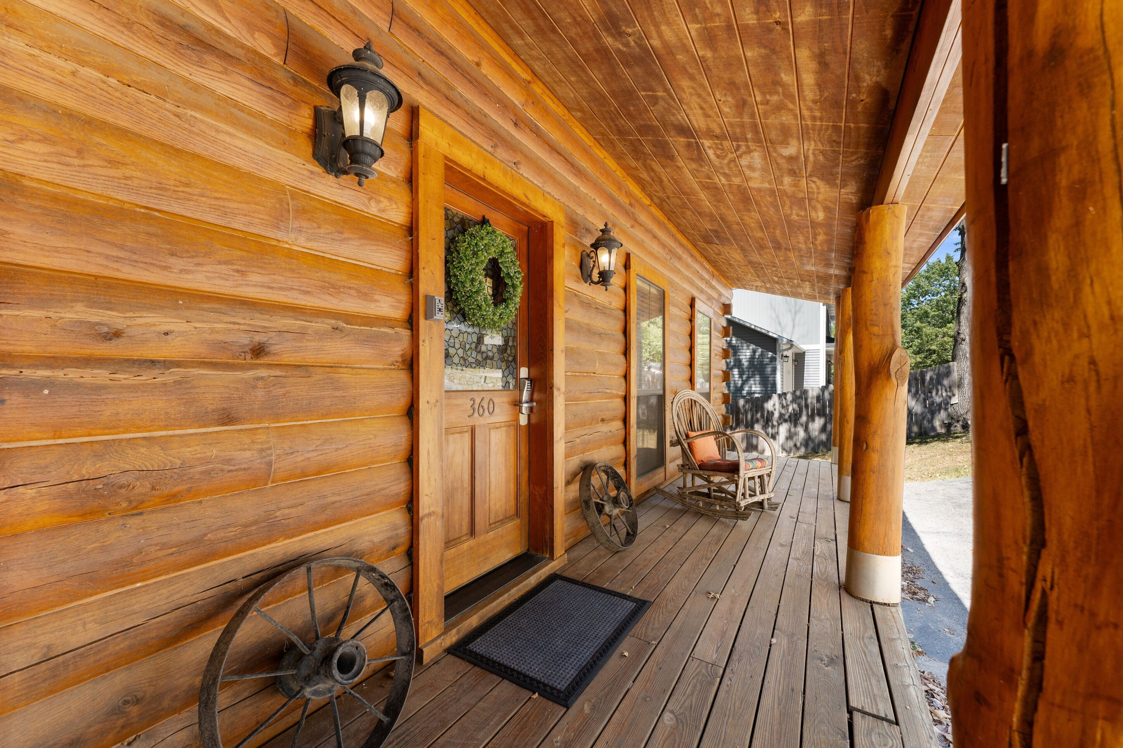 A wooden cabin with a porch, a door with a number plate, and a stone wall with a wreath.