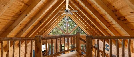 A wooden interior with a high ceiling, wooden beams, and a central staircase leading to an upper level.