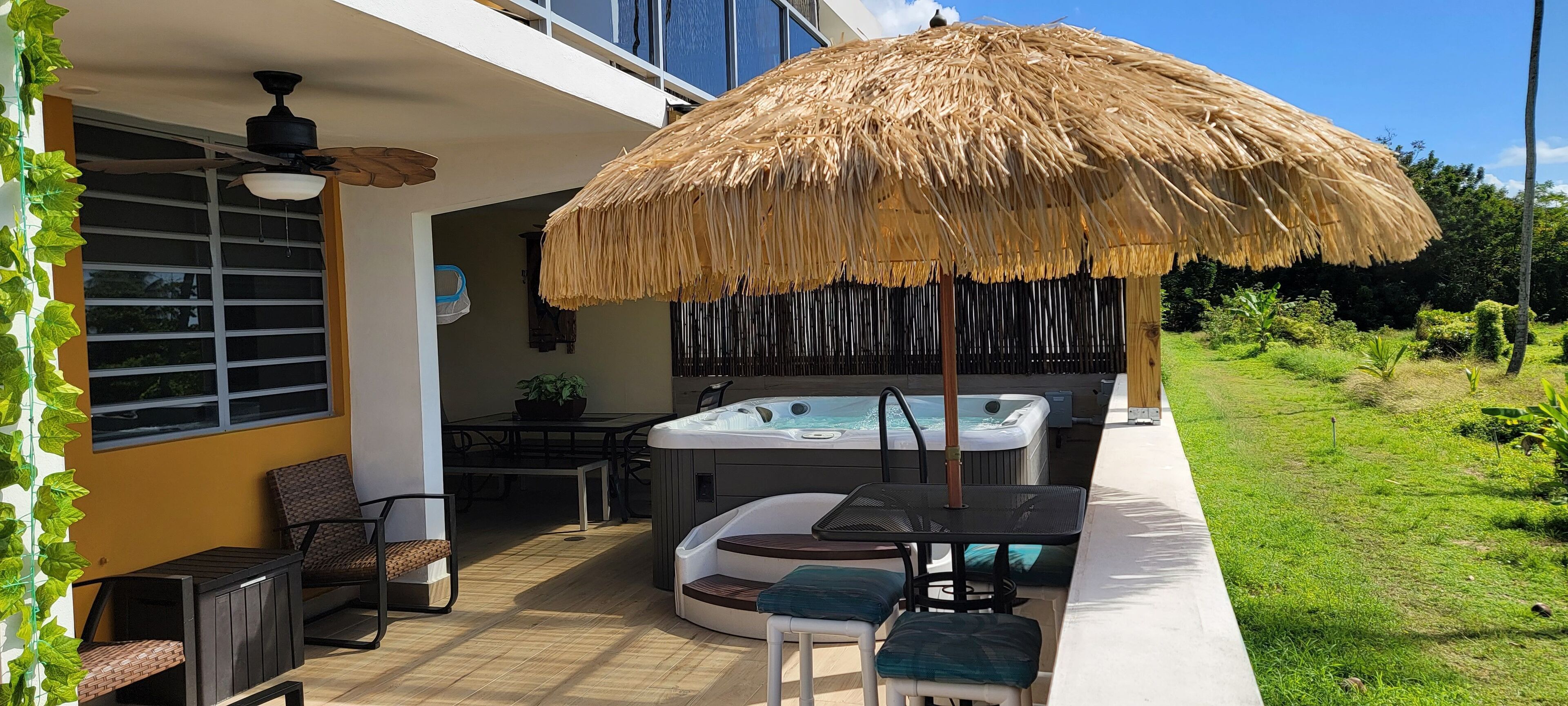 An outdoor patio with a thatched umbrella, a hot tub, and seating area.