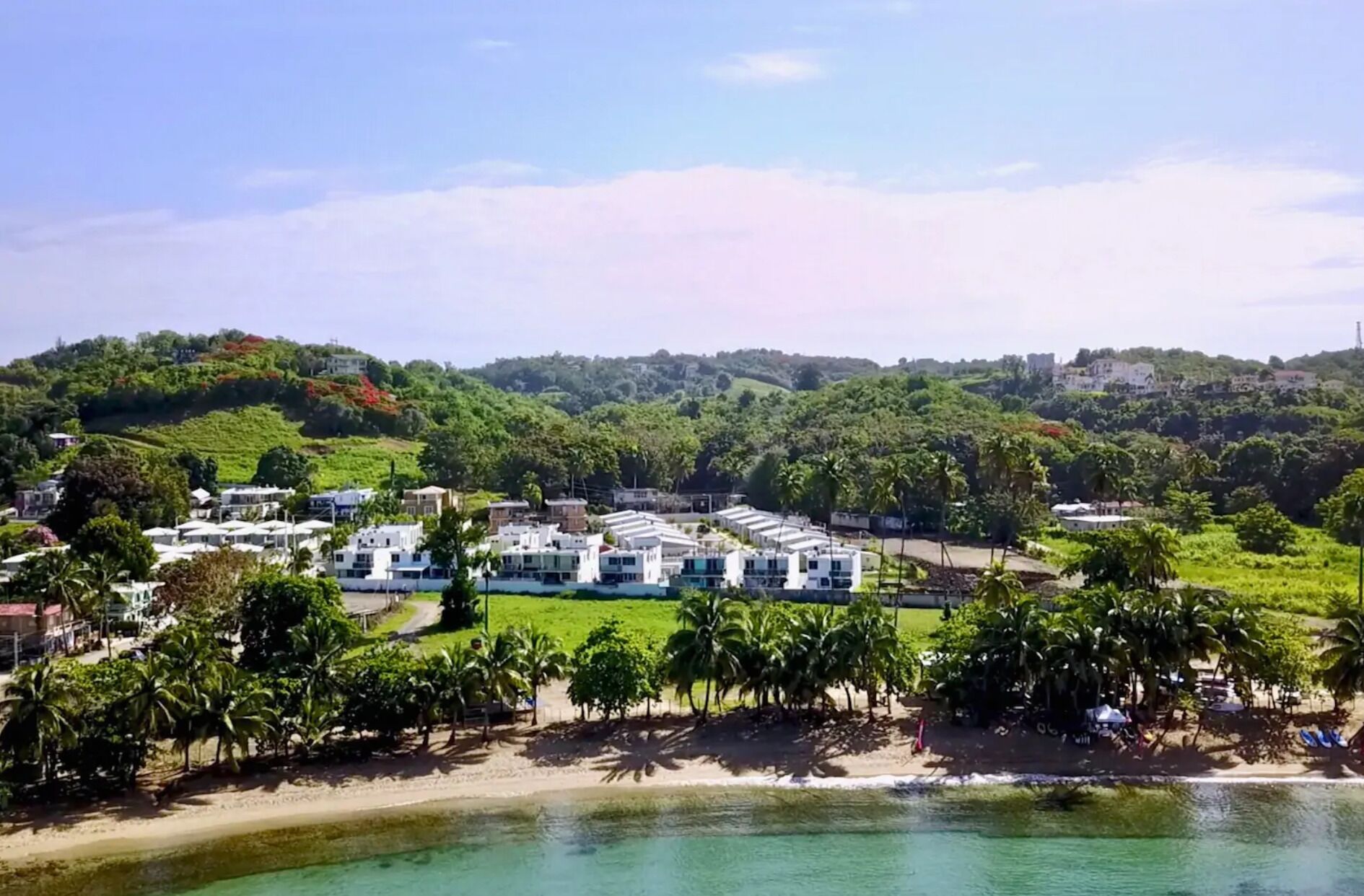 Un complejo turístico costero con varias edificaciones blancas, una playa de arena y exuberante vegetación.