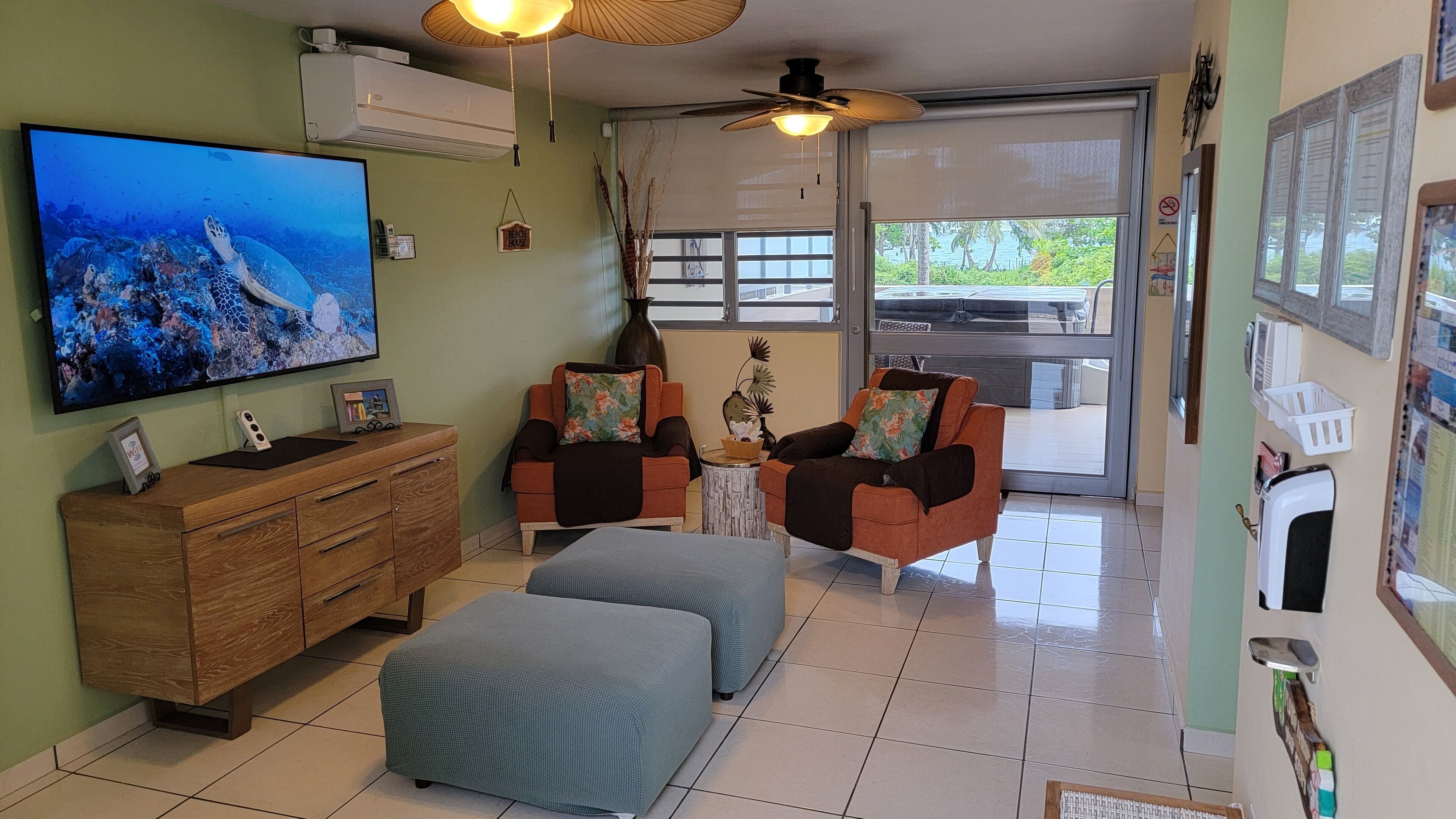 A living room with a television, a wooden cabinet, two armchairs, a small table, and a ceiling fan.
