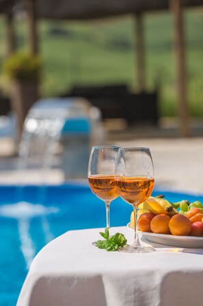Two glasses of wine on a table by a pool with a plate of fruit. - Agriturismo Molino Nuovo (Castel San Pietro Terme)
