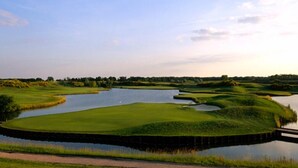Un parcours de golf avec un étang, entouré de pelouses et d’arbres.