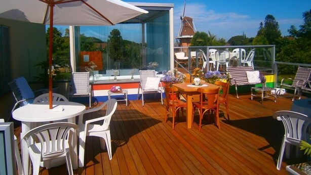 Une terrasse en bois avec des meubles d’extérieur, notamment une table et des chaises, ainsi qu’un grand parasol.