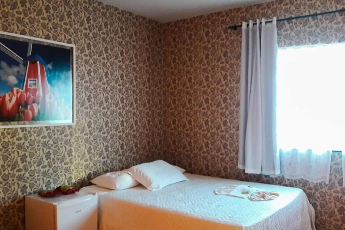 A room with a bed, a small table, a lamp, and a painting on the wall.