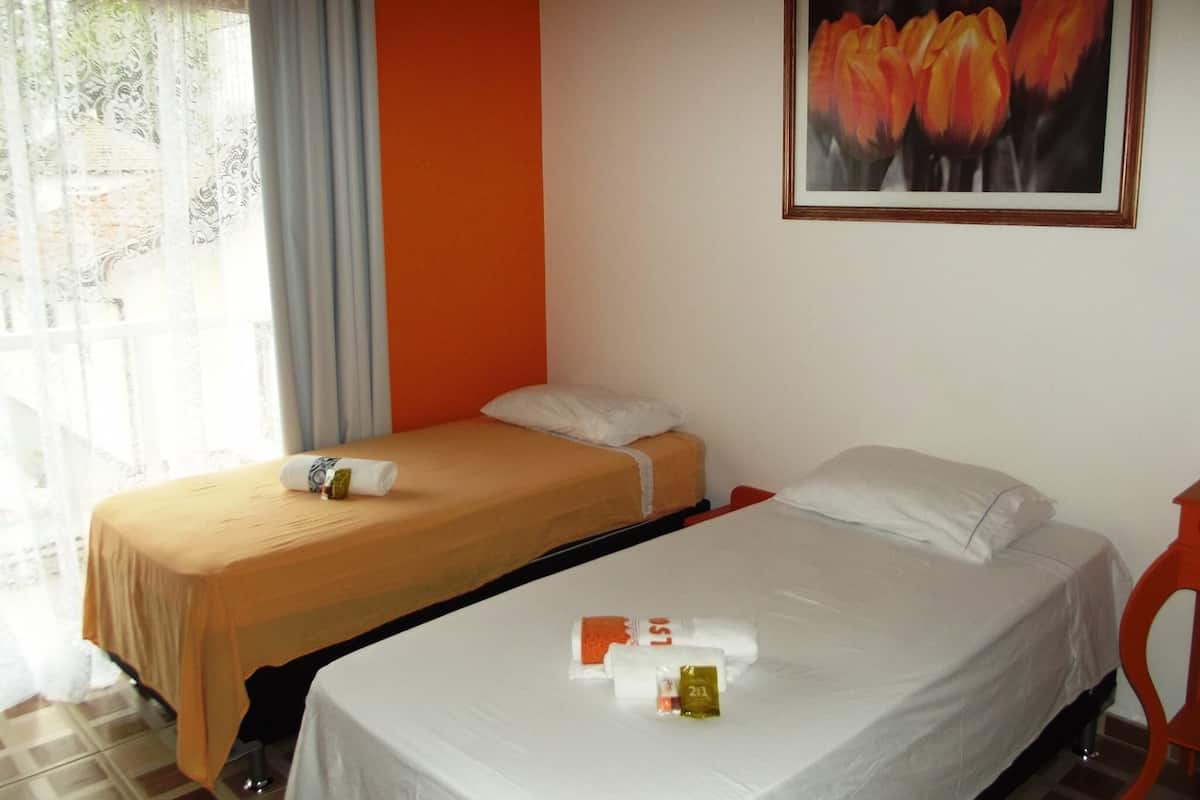 A hotel room with two beds, a window with curtains, a painting of flowers on the wall, and toiletries on the beds.