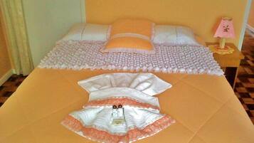 Uma cama com edredom rosa e branco, um travesseiro rosa e uma pequena mesa de cabeceira com uma luminária.