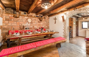 Enjoy meals in this cozy dining area with a wooden table and bench, brick wall, and stone fireplace.