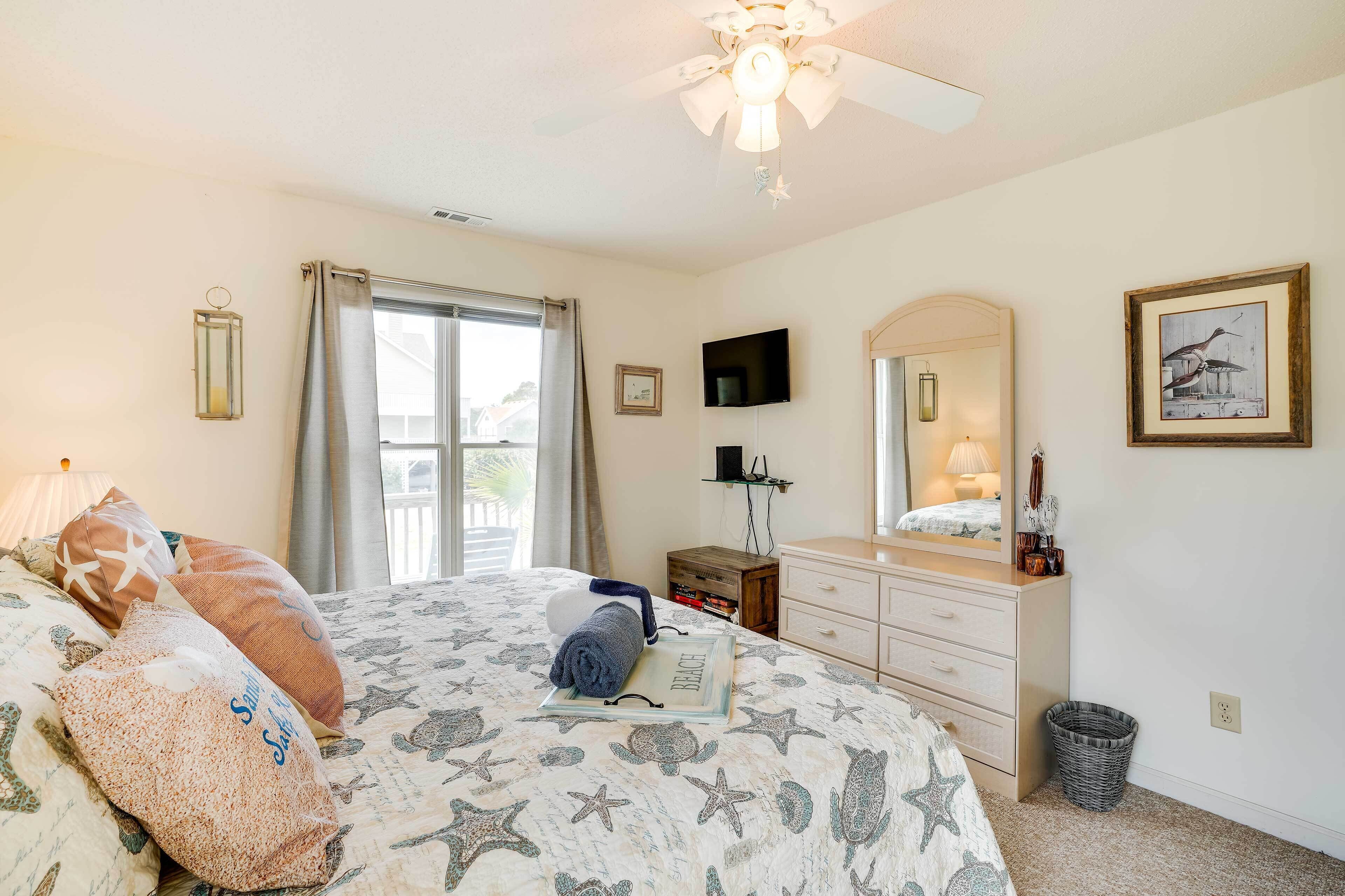 Une chambre à coucher avec un lit, une commode, un téléviseur et une fenêtre avec des rideaux.
