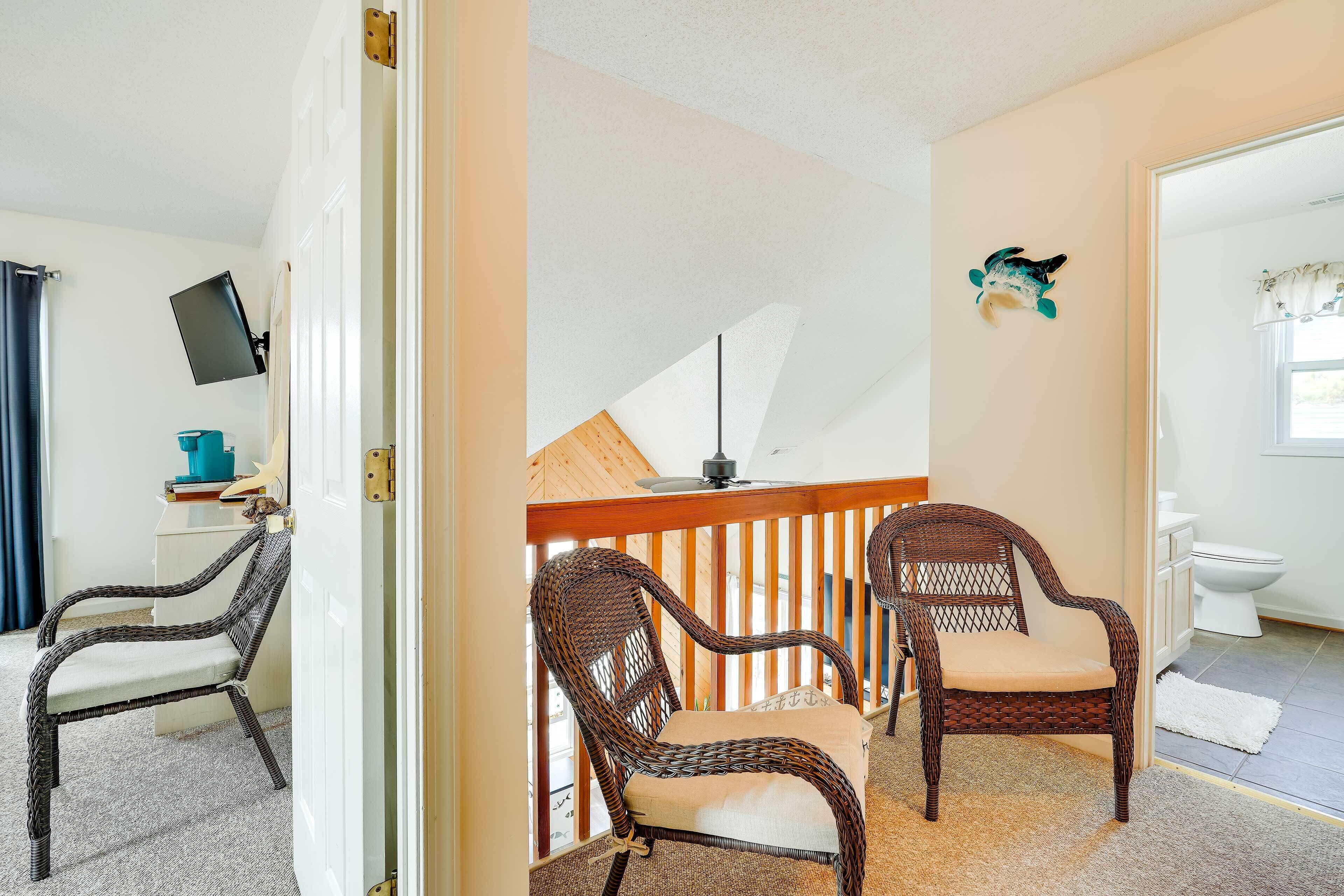 Une pièce avec deux fauteuils en osier, une rambarde en bois, un ventilateur de plafond et une petite table sur laquelle se trouve un objet bleu.