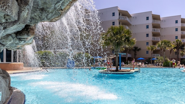 Una piscina con fontana ornamentale, circondata da palme e un edificio a più piani sullo sfondo.
