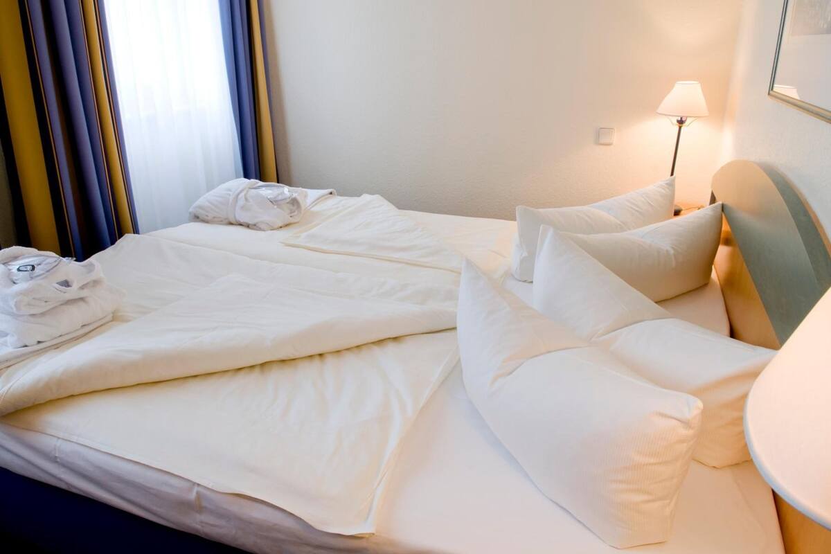 A neatly made bed with white linens and pillows, a bedside lamp, and a wall-mounted picture frame.