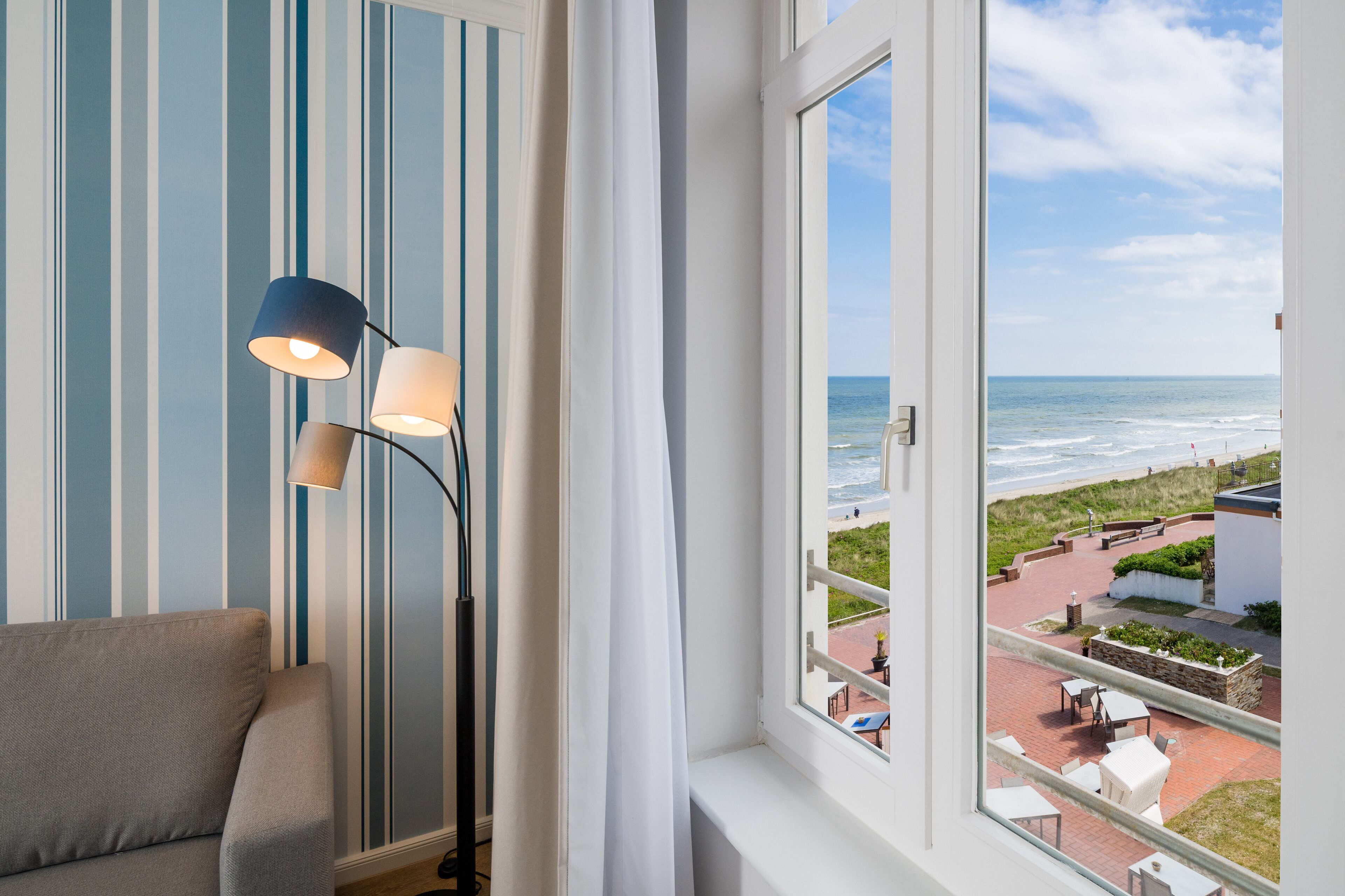 A room with a view of the beach, a sofa, and two lamps.