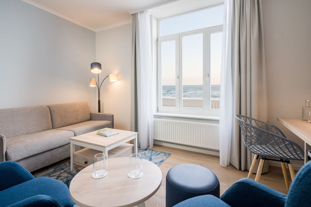 A modern living room with a sofa, a round table, and a view of the sea through a large window.